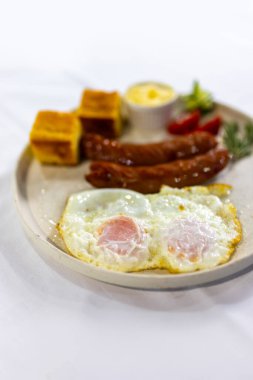 Izgara sosis, krema, ekmek, taze domates ve salatalık ile servis edilen yumurta klasik, doyurucu bir kahvaltı tabağı..
