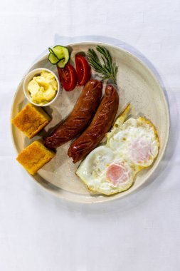 Izgara sosis, krema, ekmek, taze domates ve salatalık ile servis edilen yumurta klasik, doyurucu bir kahvaltı tabağı..