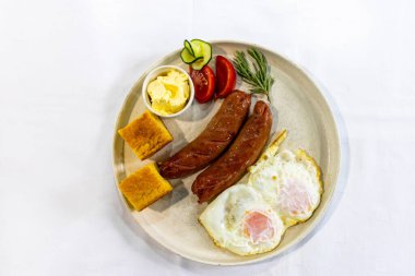 Izgara sosis, krema, ekmek, taze domates ve salatalık ile servis edilen yumurta klasik, doyurucu bir kahvaltı tabağı..
