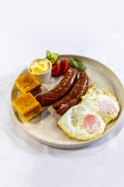 Izgara sosis, krema, ekmek, taze domates ve salatalık ile servis edilen yumurta klasik, doyurucu bir kahvaltı tabağı..