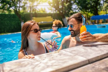 Gençler havuzda güneşli bir yaz gününün tadını çıkarıyorlar. Bir kız ve erkek arkadaşının yüzen ve rahatlatan arkadaşlarıyla birlikte mor kokteyller içip gülmelerine odaklanıyorlar..