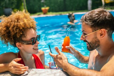Gençler havuzda güneşli bir yaz gününün tadını çıkarıyorlar; erkek arkadaşıyla yüzen arkadaşlarıyla birlikte mor kokteyl içen afro saçlı kıza odaklanıyorlar..