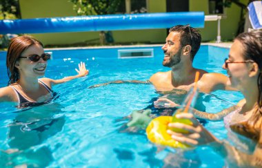Bir grup genç arkadaş sıcak bir yaz günü havuzda eğleniyor; bir kız şamandırada, diğerleri etrafında, hepsi kokteyl içiyor ve birlikte keyifli, rahatlatıcı zaman geçiriyorlar..