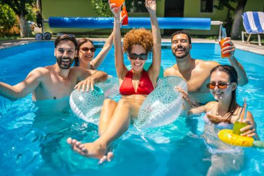 Bir grup genç arkadaş sıcak bir yaz günü havuzda eğleniyor; bir kız şamandırada, diğerleri etrafında, hepsi kokteyl içiyor ve birlikte keyifli, rahatlatıcı zaman geçiriyorlar..