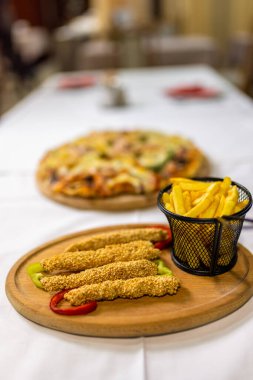 Kızarmış tavuk çubukları, altın kızartmalar ve zeytin, jambon ve mantarla kaplanmış peynirli Pizza Capricciosa içeren ağız sulandırıcı bir ziyafet. Paylaşım için mükemmel..