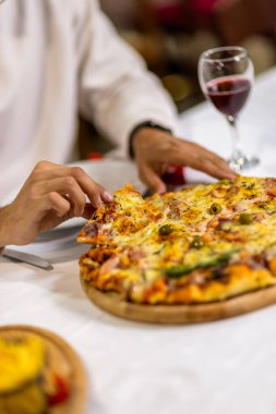 Bir bardak kırmızı şarabın yanında bir dilim pizza alarak, samimi bir restoran atmosferinde servis edilir, otantik bir İtalyan yemek deneyimi için mükemmel..