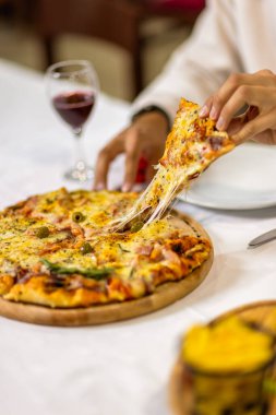 Bir bardak kırmızı şarabın yanında bir dilim pizza alarak, samimi bir restoran atmosferinde servis edilir, otantik bir İtalyan yemek deneyimi için mükemmel..