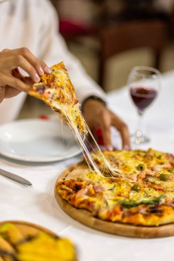 Bir bardak kırmızı şarabın yanında bir dilim pizza alarak, samimi bir restoran atmosferinde servis edilir, otantik bir İtalyan yemek deneyimi için mükemmel..