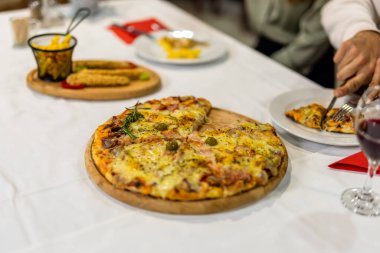 Sıcak bir restoran atmosferinde servis edilen kırmızı şarabın yanında bir dilim pizza Capricciosa, otantik bir İtalyan yemek deneyimi için mükemmel..