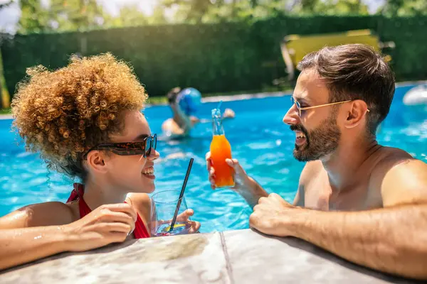 Gençler havuzda güneşli bir yaz gününün tadını çıkarıyorlar; erkek arkadaşıyla yüzen arkadaşlarıyla birlikte mor kokteyl içen afro saçlı kıza odaklanıyorlar..