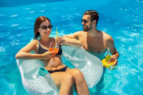 Genç çift güneşli bir yaz gününde havuzda dinleniyor; kız şamandıranın üzerinde, oğlan onun yanında ve ikisi de renkli kokteyller içiyor ve eğleniyorlar..