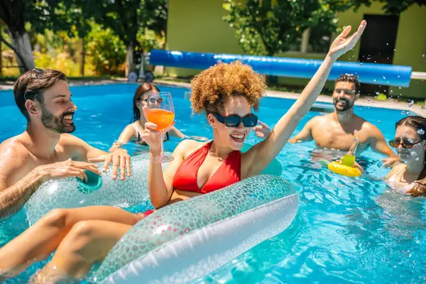 Bir grup genç arkadaş sıcak bir yaz günü havuzda eğleniyor; bir kız şamandırada, diğerleri etrafında, hepsi kokteyl içiyor ve birlikte keyifli, rahatlatıcı zaman geçiriyorlar..