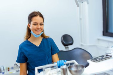 Modern klinikte mavi ceket ve yüz maskesi takan kadın dişçi diş aletlerini hazırlıyor. Hijyen, hazırlık ve profesyonel bakım kavramı