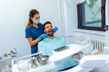 Modern klinikte erkek hastaya diş tedavisi uygulayan kadın diş hekimi. Profesyonel bakım, hassasiyet ve oral sağlığa odaklanın..