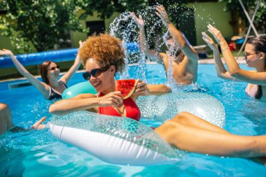 Havuzda yüzen ve karpuz yiyen genç bir kadın. Etrafı arkadaşlarla çevrili. Havuzda eğleniyorlar.. 