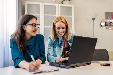  Kadın CEO, modern bir ofiste çalışan meslektaşına görevlerini anlatıyor. Takım çalışması, rehberlik ve profesyonel işbirliği sergiliyor..