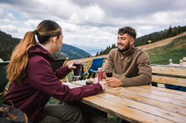 Yürüyüşten sonra dağların tepesindeki bir restoranda dinlenen iki yürüyüşçü taze meyve suyu içip doğanın çarpıcı panoramik manzarasının tadını çıkarıyorlar..
