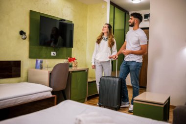 Genç bir çift otel odasına bavullarıyla giriyor, gezilerinde güzel bir şekilde hazırlanan odadan etkileniyor ve memnun kalıyorlar..