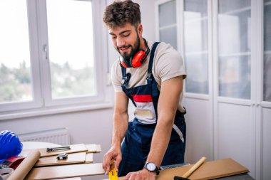 Tamirci, ekipman ve güvenlik teçhizatlarıyla donatılmış bir apartmanın döşemelerini dikkatlice lamine ediyor..