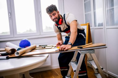 Tamirci, ekipman ve güvenlik teçhizatlarıyla donatılmış bir apartmanın döşemelerini dikkatlice lamine ediyor..