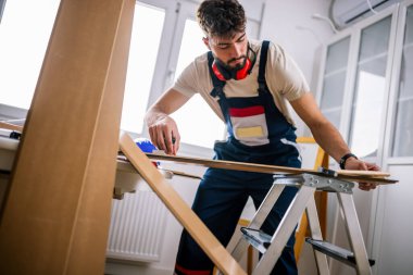 Tamirci, ekipman ve güvenlik teçhizatlarıyla donatılmış bir apartmanın döşemelerini dikkatlice lamine ediyor..