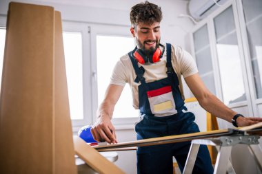 Tamirci, ekipman ve güvenlik teçhizatlarıyla donatılmış bir apartmanın döşemelerini dikkatlice lamine ediyor..