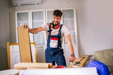 Bir dairedeki tamirci, zemini hassas ve profesyonel aletlerle onarmaya hazırlanan lamine bir kalas tutuyor..