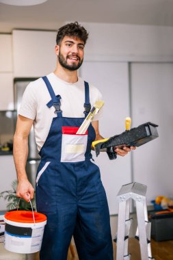 Bir dairedeki ressam, duvarları boyamaya hazırlanıyor, elinde kireç ve fırça tutuyor, yenilenmeye hazır..
