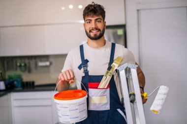 Bir dairedeki ressam, duvarları boyamaya hazırlanıyor, elinde kireç ve fırça tutuyor, yenilenmeye hazır..