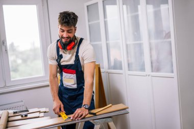 Tamirci, ekipman ve güvenlik teçhizatlarıyla donatılmış bir apartmanın döşemelerini dikkatlice lamine ediyor..