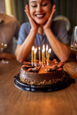Doğum günü kızı, arkadaşlarıyla, hediyelerle ve şenlikli dekorasyonlarla çevrili bir restoranda pastasına mum üflerken gülümsüyor..