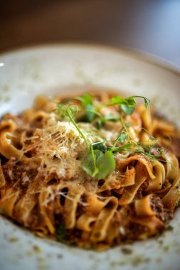 Klasik İtalyan tagliatelle bolonez makarnası bir restoranda bir tabakta servis edilir, zengin et sosu ve taze garnitür..