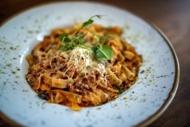 Klasik İtalyan tagliatelle bolonez makarnası bir restoranda bir tabakta servis edilir, zengin et sosu ve taze garnitür..