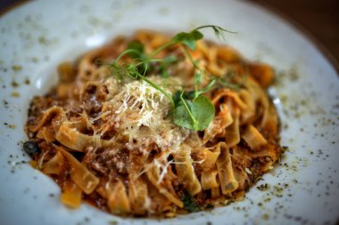 Klasik İtalyan tagliatelle bolonez makarnası bir restoranda bir tabakta servis edilir, zengin et sosu ve taze garnitür..