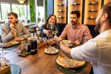 Bir grup iş arkadaşı bir restoranda şarapla tezahürat yaparken pizza, makarna, tavuk ve pirinç yiyor, gülümsüyor ve iş hakkında konuşuyor..