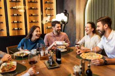 Bir grup iş arkadaşı bir restoranda öğle yemeği, bir kadın yemek teklif ederken masa pizza, makarna, tavuk, pilav ve şarapla dolu..