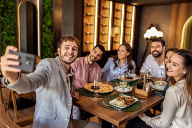 Bir grup iş arkadaşı birlikte bir restoranda yemek yerken hatıralarını çekmek için selfie çekiyorlar..