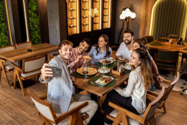 Bir grup iş arkadaşı birlikte bir restoranda yemek yerken hatıralarını çekmek için selfie çekiyorlar..