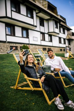 Mutlu genç çift, sonbaharda otelin önünde dinlenirken birlikte selfie çekiyorlar, rahat ve romantik sonbahar anlarının tadını çıkarıyorlar..