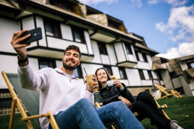 Mutlu genç çift, sonbaharda otelin önünde dinlenirken birlikte selfie çekiyorlar, rahat ve romantik sonbahar anlarının tadını çıkarıyorlar..