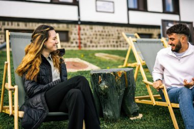 Mutlu genç çift sonbahar boyunca otelin önündeki dinlenme yerlerinde kahve ve meyve suyu içiyor, huzurlu ve romantik bir sonbahar tatili..