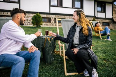Mutlu genç çift sonbahar boyunca otelin önündeki dinlenme yerlerinde kahve ve meyve suyu içiyor, huzurlu ve romantik bir sonbahar tatili..