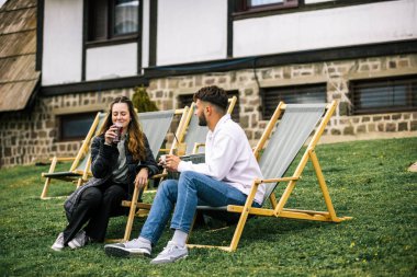 Mutlu genç çift sonbahar boyunca otelin önündeki dinlenme yerlerinde kahve ve meyve suyu içiyor, huzurlu ve romantik bir sonbahar tatili..