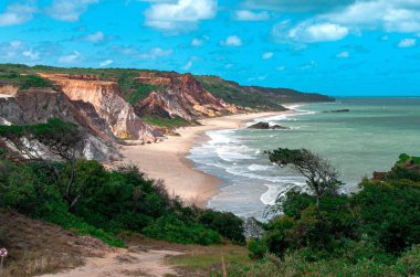 Tepenin tepesinden, deniz ve mavi gökyüzü ile çarpıcı bir kontrast yaratan güzel bir sahil ve uçurumlar görüyoruz..