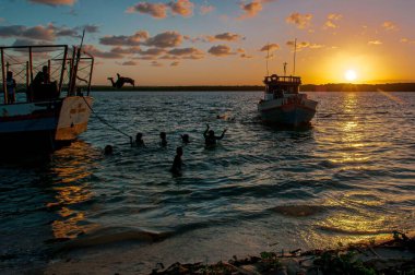 Sahilde, demirlemiş tekneler ve birkaç kişi oynuyordu. Gün batımında tekneden atlayıp manzarayı aydınlatıyorlardı..