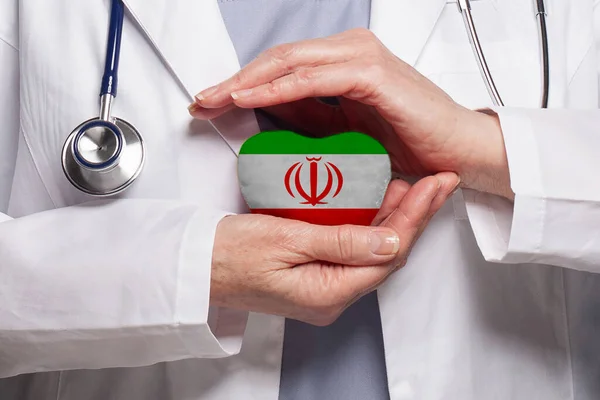 Iranian doctor holding heart with flag of Iran background. Healthcare, charity, insurance and medicine concept