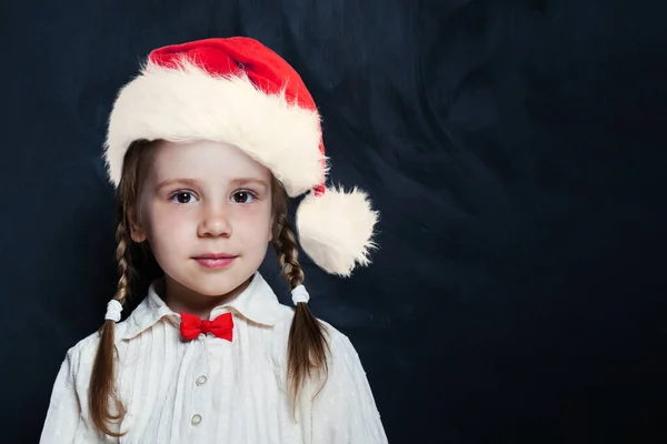 サンタの帽子のかわいい女の子 コピースペース付きの空の黒板の背景に幸せな子供 学校に戻る — ストック写真