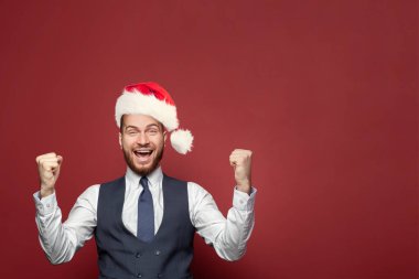 Noel şapkalı mutlu işadamı kırmızı afiş arkaplanındaki portreye gülüyor.