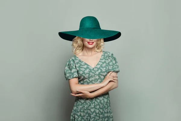 stock image Beautiful woman with makeup and blonde curly hair wearing green wide broad brim hat against light green background