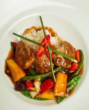 Ekşi etli ve sebzeli pirinç ve beyaz tabakta tatlı sosis.